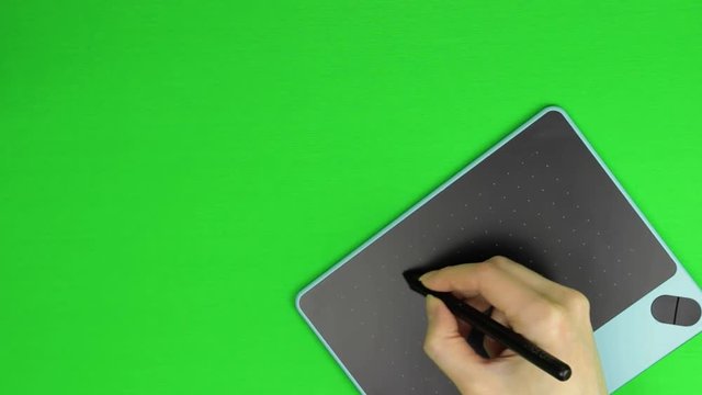 Female hand working on black and blue graphic tablet using stylus on green screen. Sketching, design and art. Chroma key, top view.