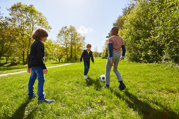 Fototapeta premium Three kids play football together in the park