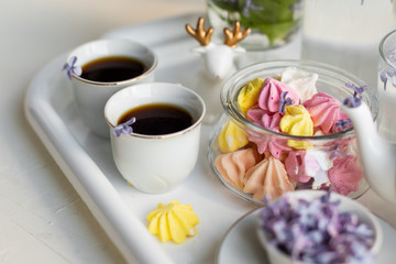 Breakfast with black tea or coffee and meringue kisses on the white table. Spring lilac flowers in a glass vase.