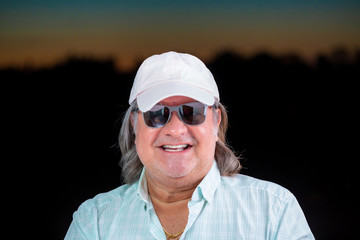 Man portrait outside during dusk hours. The horizon serves as background. He is smiling and looking to the camera.