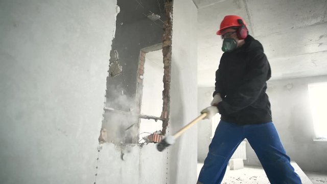 demolition work and rearrangement. worker with sledgehammer at wall destroying
