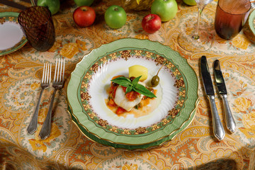 white fish with potatoes, basil and olive with sauce on a plate  and on a table. front view
