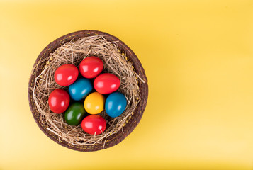 Wicker basket of colorful Easter eggs isolated on yellow