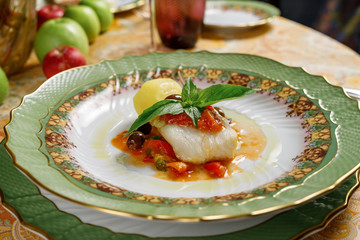 white fish with potatoes, basil and olive on green plates. front view