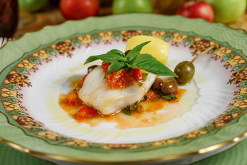 white fish with potatoes, basil and olive with sauce on green plates. front view
