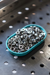 A handful of metal nuts in a plastic container for storage