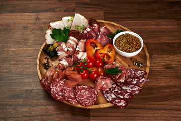many types of sausages with vegetables and olives on a wooden plate. top view