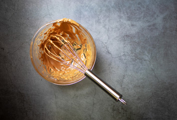 Whisking melted chocolate with cream; stain in a glass mixing bowl on table background.