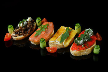 assorted bruschetta with red fish, fried mushrooms, cheese, dill cherry tomato, cucumber, arugula, on a black background