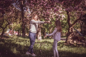 Naklejka na ściany i meble Sakura blossomed. Young mother with her child have fun in the park near the sakura. Spring morning. They look at each other