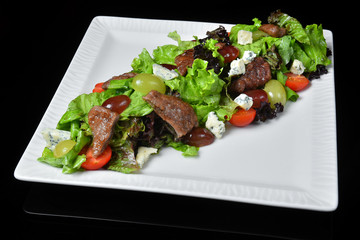 Salad with herbs, meat, cheese, tomatoes, grapes, Basil, lettuce leaves on a white plate