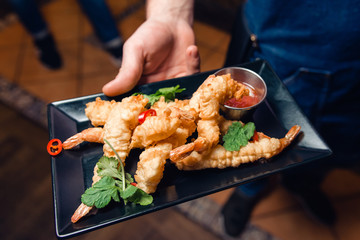 Shrimp tails in crispy breading with hot sweet sauce and parsley on a black plate