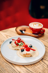 
pancakes with white cream strawberries currants mint raspberries on a white plate