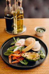 
Bun with red fish, avocado, lemon, mint, on a black plate