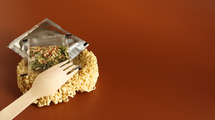 Obraz na płótnie Canvas Raw instant noodles in the shape of a circle with a wooden fork and aromatic seasonings and butter. pasta, for the preparation of which it is enough to pour boiling water and wait a few minutes