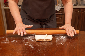 female hands roll out the pizza dough on a wooden table in the home kitchen. homemade food