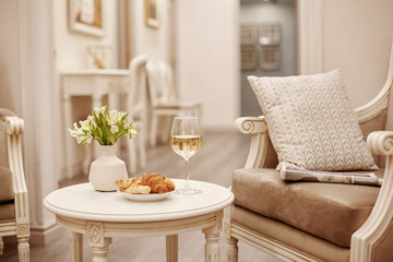 A glass of white wine, crispy croissants and a vase of white flowers sit on the table in the cozy living room