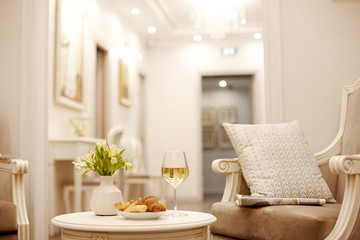 A glass of white wine, crispy croissants and a vase of white flowers sit on the table in the cozy living room