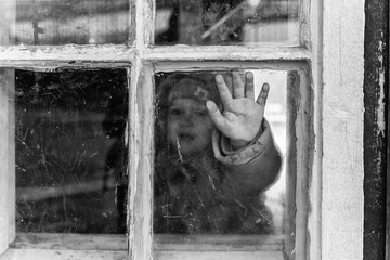 the hand of a small child behind a scratched window. Dressed child in the image of an orphan. Old wooden house