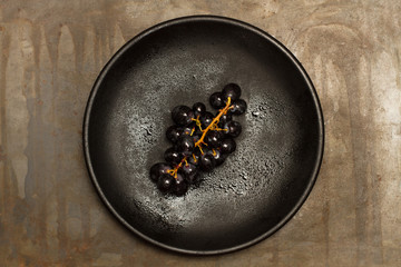Uvas negras sobre un plato redondo negro sobre un fondo de metal oscuro. Vista superior