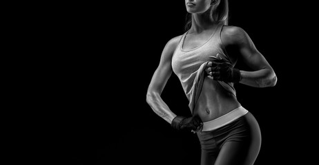 Fototapeta na wymiar Fitness woman in sports tank top, gloves. Black and white close-up photo. Fitness athletic young woman showing her well trained body, six pack, perfect abs, shoulders, biceps, triceps and chest.