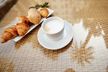 Fresh pastries and a Cup of hot coffee are on the table on the terrace, next to a sprig of olive. View from, space for text