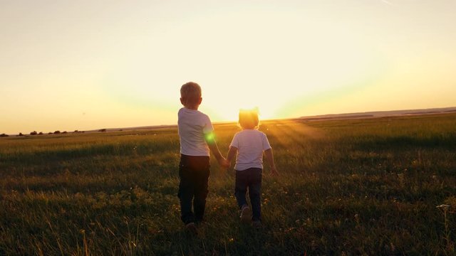Children boy and girl walking on the green grass holding hands.