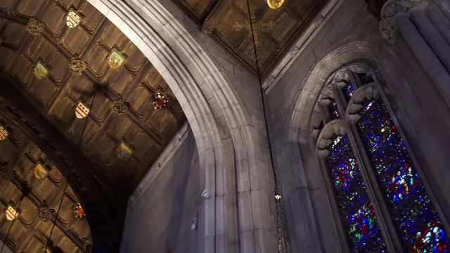 Camera pans across vaulted cathedral ceiling with wooden panels, and stained glass gothic windows with tracery.