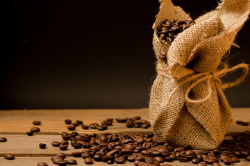 Naklejka premium Wypalone ziarna czarnej kawy, rozsypujące się z worka jutowego na surowe deski.
