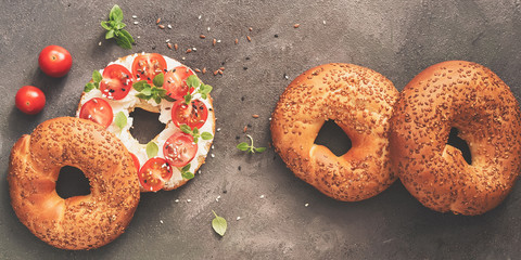 Homemade bagel sandwich with soft cheese, cherry tomatoes and basil on a dark background, border. Top view, flat lay,border. Toned photo