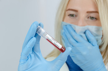 young female nurse in a medical mask and blue gloves holds a positive test result for coronavirus in close-up and covers her mouth with her hands, the concept of medicine