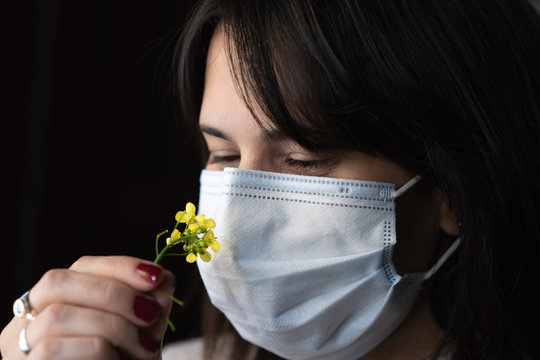 mujer oliendo una flor con un barbijo en cuarentena woman smelling a flower with a chin mask