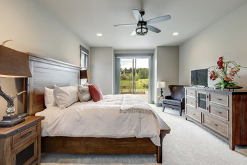 Natural tone luxury bedroom interiors in new American vacation home. Wood furniture and beige carpet.