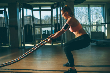 Fototapeta na wymiar Young woman with battle ropes exercise in the fitness gym