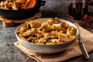 Homemade pasta with green peas, chicken and sauce on a dark background