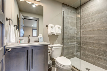 Natural new classic bathroom interior with new glass and ceramic tiles walk in shower and grey walls with towels.