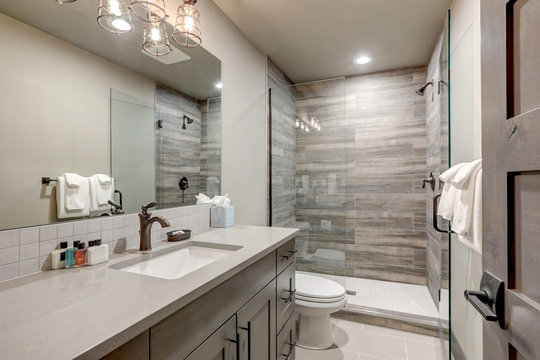 Natural new classic bathroom interior with new glass and ceramic tiles walk in shower and grey walls with white towels.