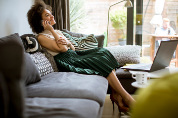 Fototapeta premium Young curly hair african woman relaxing at home and using mobile phone