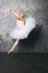 Fototapeta premium Pretty young ballerina dancer dancing classical ballet against rustic wall