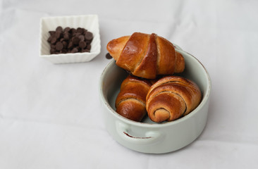 homemade whole spelled flour croissants, in a small ceramic pot next to chocolate chips, on a white background