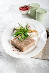 Jellied meat with fresh herbs and mustard on a white plate