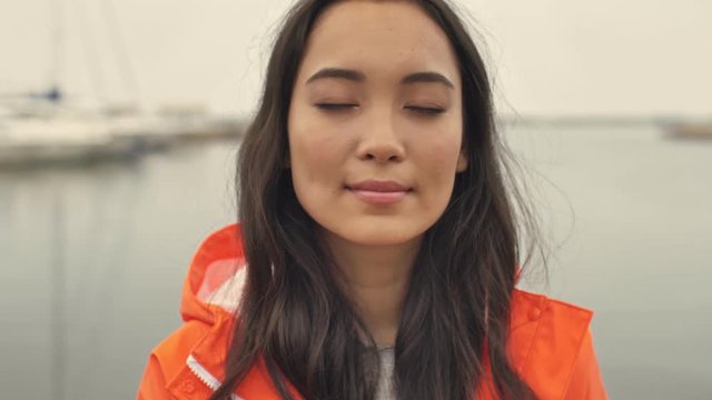 Amazing asian  woman walking by harbor grant outdoors in orange coat.