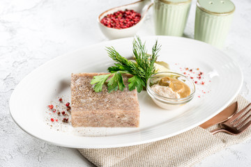 Jellied meat with fresh herbs and mustard on a white plate