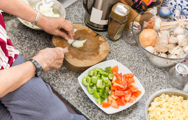 Top view of senior woman hands chopping onion on wooden board in the kitchen.