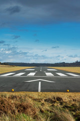 Small airport asphalt runway with markings for landings. Blue cloudy sky and fields around. Nobody.