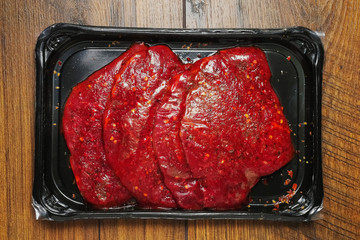 Fresh thin sliced steak marinated in plastic packaging without label on a wooden table surface, top view, Retail product.