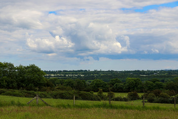 Fototapeta na wymiar View over the fertile rural agricultural landscape of County Meath, Ireland in summer with its patchwork of rich green fields divided by the lush tree lined hedgerows and blue cloudy sky above