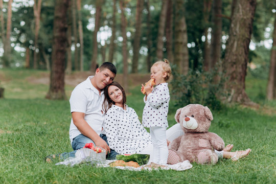 Mom, dad and little daughter on the picnic with teddy bear in the park outdoors. The concept of summer holiday. Mother's, father's, baby's day. Family spending time together on nature. Family look