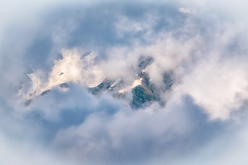 High mountain peak with snow hidden in clouds and fog