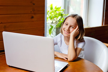 Home schooling. A girl is sitting at a table with a laptop during an online video chat of a school lesson with a teacher and class. Concept of distance education. Self-isolation in quarantine